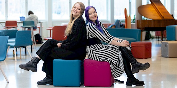 Kaksi opintosihteeriä istuu jakkaroilla ja hymyilee